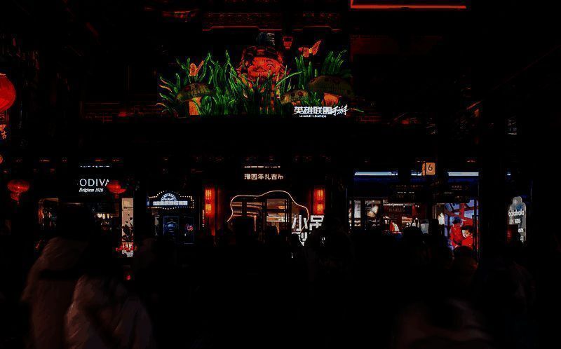 游客手持地图寻找花灯点位，背景是灯火辉煌的豫园夜景