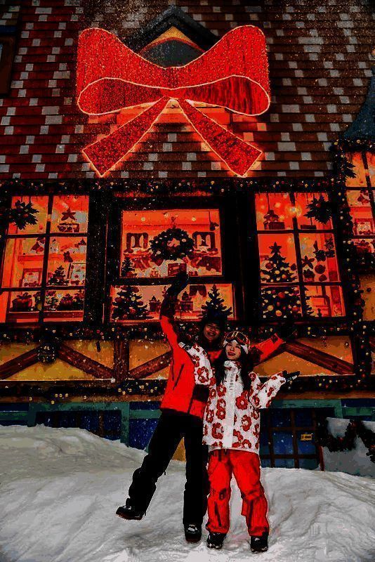 广州热雪奇迹内景，滑雪者在雪道上滑行，背景为灯光装饰的北欧风格木屋与狼人杀角色立牌，空中飘落人造雪花