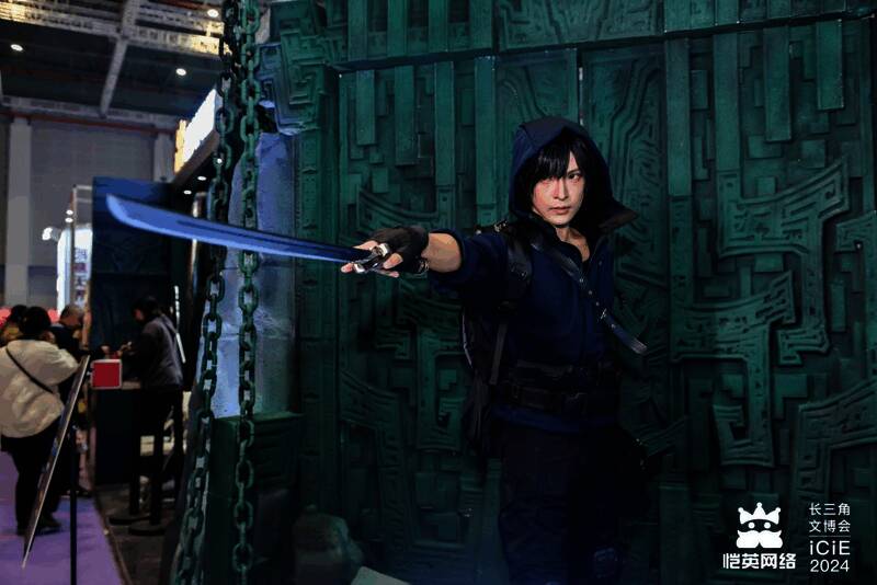 COSER扮演的张起灵与吴邪站立于展台中央，周围粉丝举手机拍摄，气氛热烈